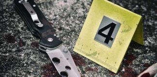 Folding knife beside evidence marker on gritty surface